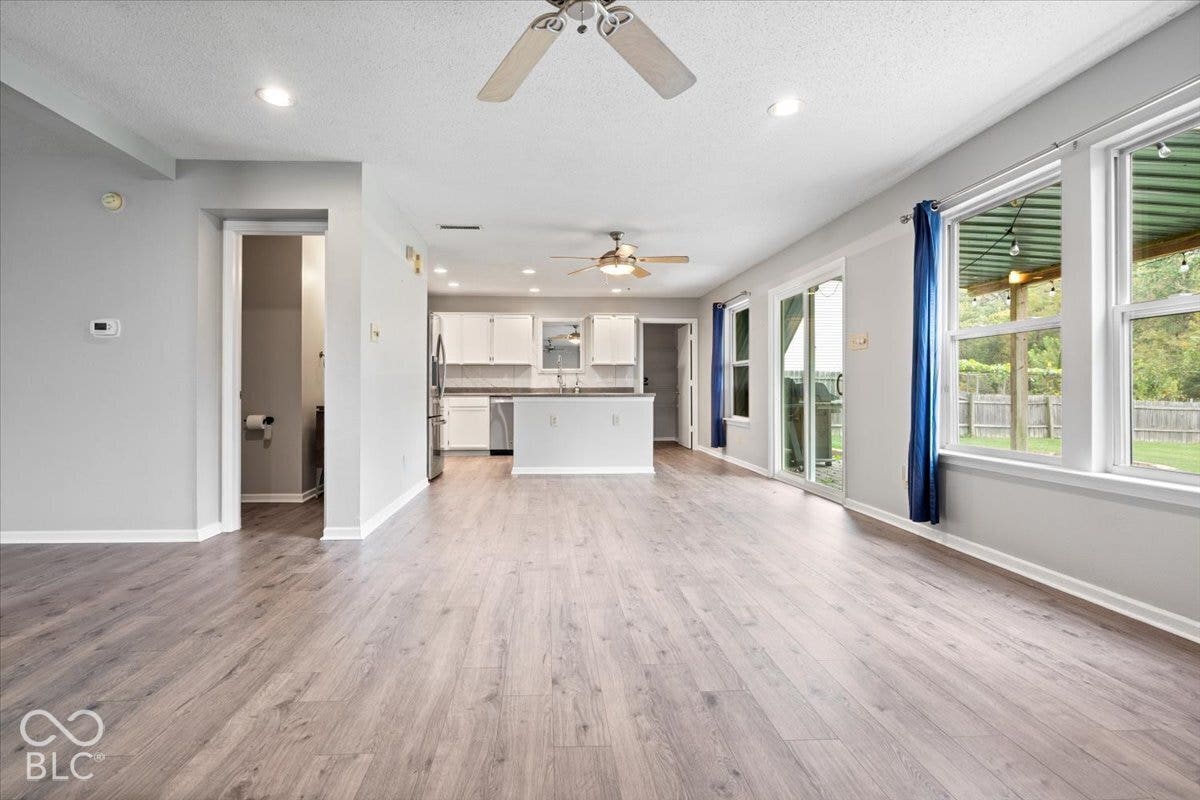 Open-concept interior featuring wood-finish flooring, recessed lighting, ceiling fans, white kitchen cabinetry, and sliding glass doors