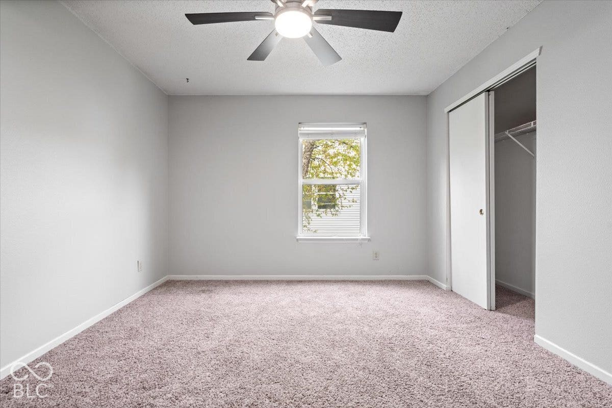 Neutral wall tones, wall-to-wall carpeting, ceiling fan with integrated lighting, window with horizontal blinds, and closet with sliding doors