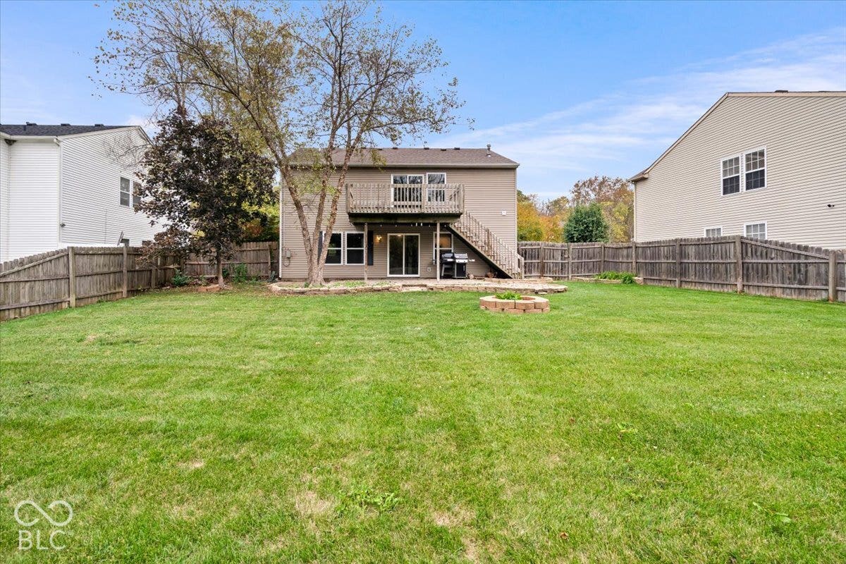 Expansive backyard featuring a wood-fenced perimeter, elevated wooden deck, stone patio, and stone-bordered fire pit