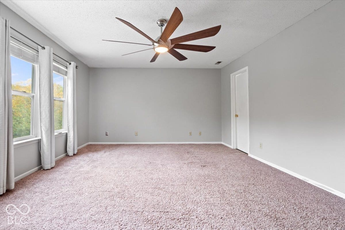 Interior space featuring neutral-toned carpeting, multi-blade ceiling fan with integrated lighting, and dual windows