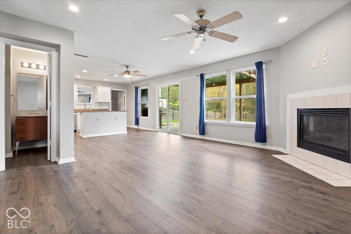 Living area featuring wood-finish flooring, a tile-surround fireplace, sliding glass doors, recessed lighting, and dual ceiling fans