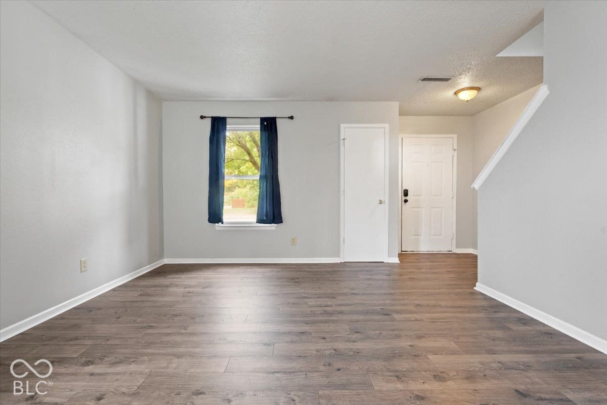 Neutral-toned interior featuring wood-finish flooring, a single-panel exterior door, and a staircase with a white handrail