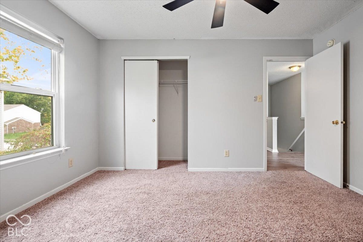 Neutral-toned walls, plush wall-to-wall carpeting, window with natural lighting, closet with sliding door, and ceiling fan fixture