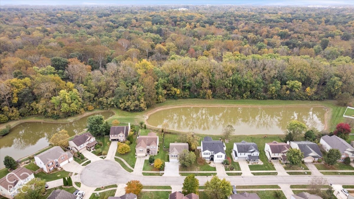 Aerial perspective of a suburban neighborhood featuring paved cul-de-sac streets, residential properties, and expansive bordering woodland with a natural pond