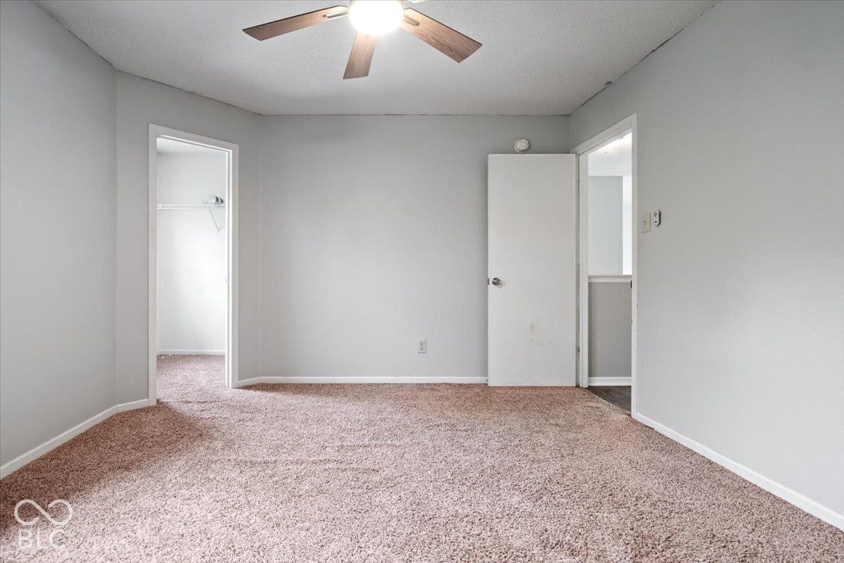 Neutral-toned wall finish, wall-to-wall carpeting, and a ceiling-mounted light fixture with a multi-blade fan