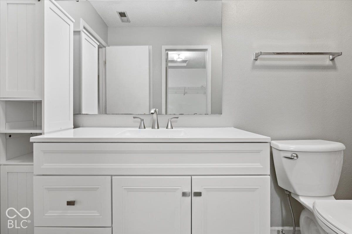White vanity featuring integrated countertop, Shaker-style cabinetry with built-in side shelving, metallic finish hardware, and wall-to-wall mirror