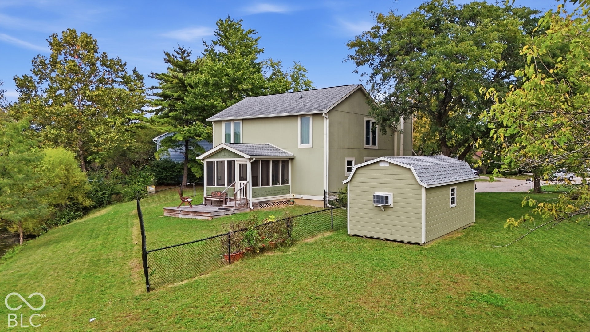 Two-story residence featuring a screened-in porch, attached wooden deck, detached storage structure with gambrel roof, and chain-link perimeter fencing situated on a grass-covered lot