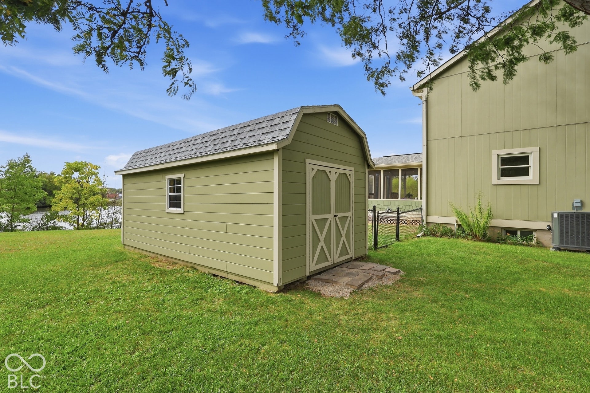 Detached storage shed with shingled roof, horizontal siding, and double doors situated on a grassy lot