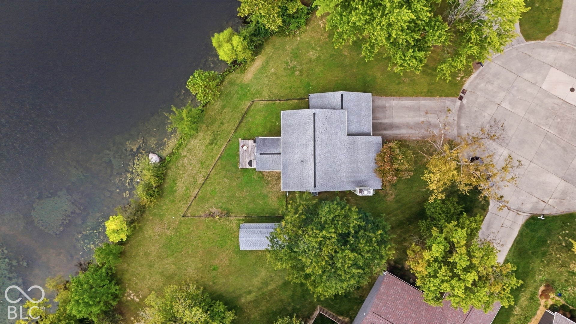 Waterfront lot featuring a multi-level deck, detached storage structure, concrete driveway, and mature landscaping