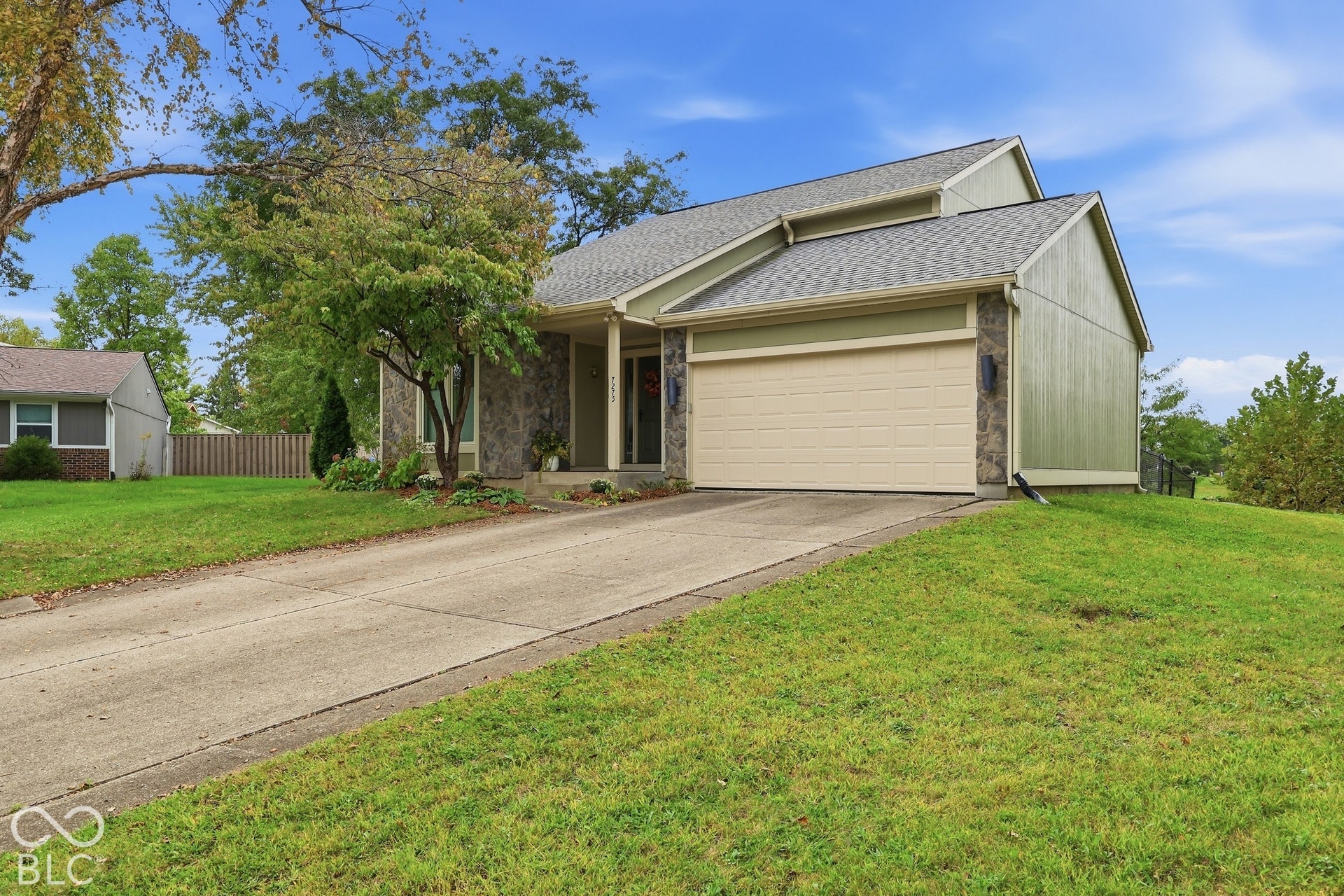 Multi-level exterior featuring vertical siding, stone masonry accents, a paved concrete driveway, and an attached two-car garage