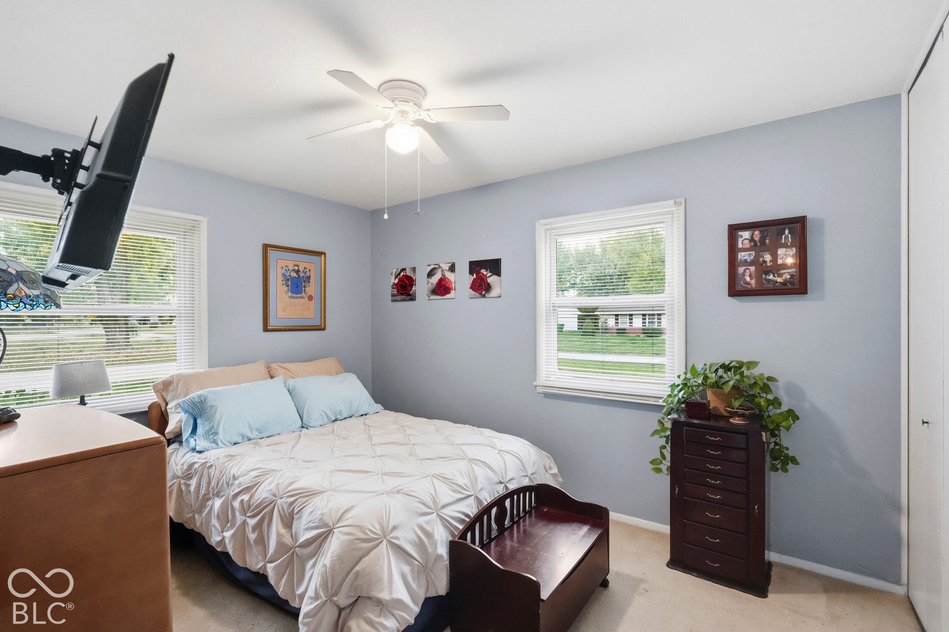 This corner bedroom has a ceiling fan with light fixture, dual windows, and closet with sliding doors. The floor is carpeted.