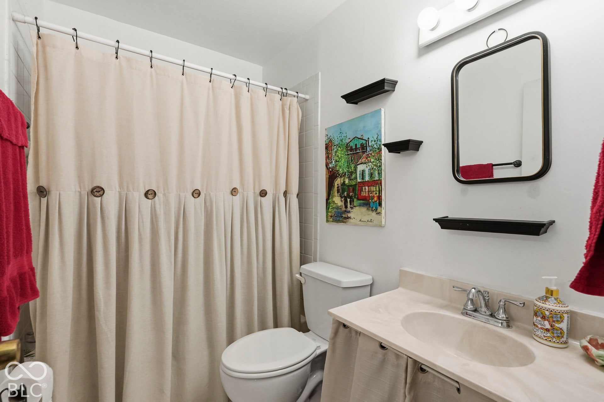 Another view of the full bathroom featuring a vanity with a light-toned countertop, integrated basin, dual-handle faucet, wall-mounted mirror, and decorative built-in wall shelving.
