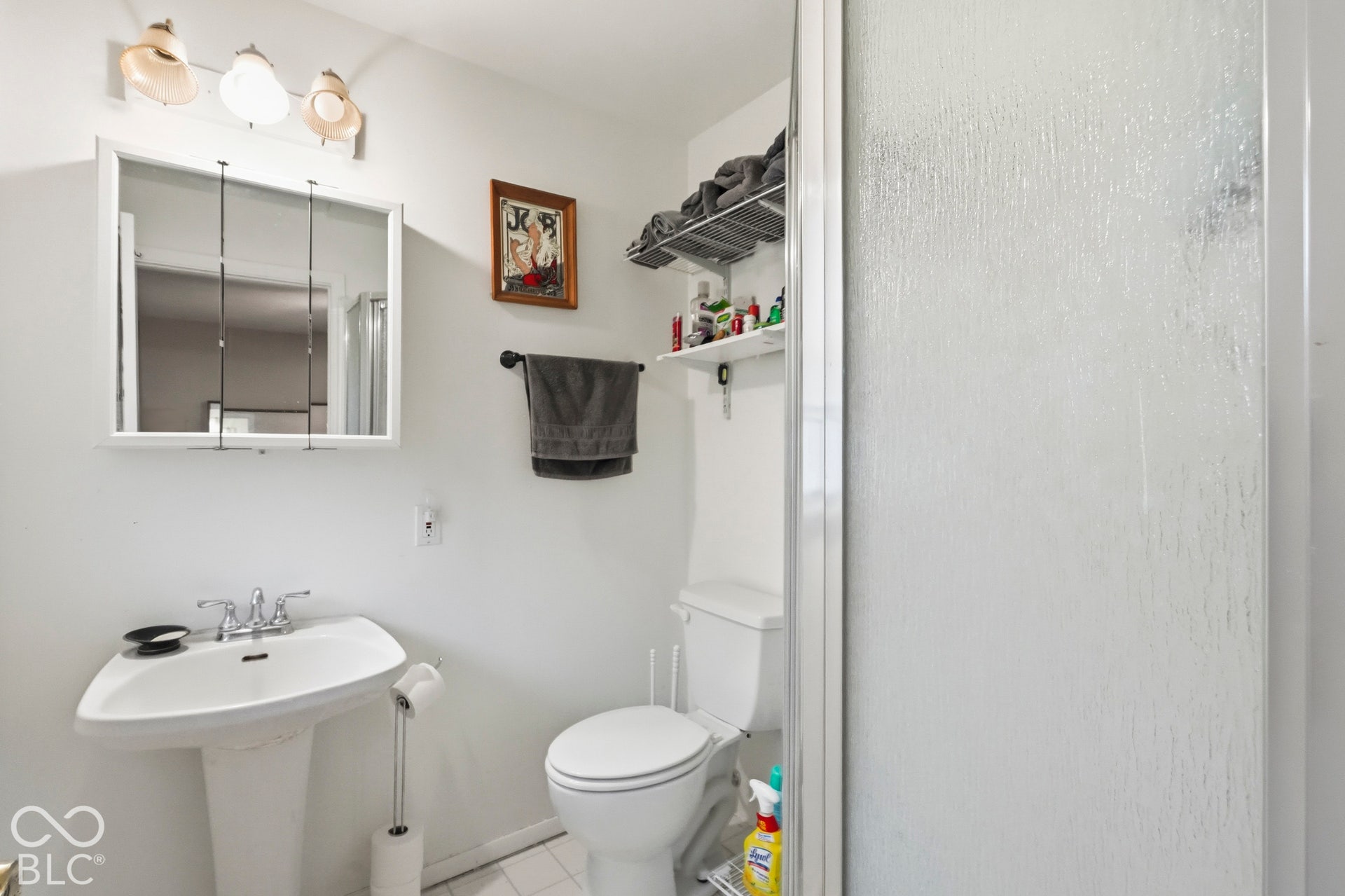 The en-suite bathroom has a wall-mounted mirrored cabinet with three-light fixture, white pedestal sink with chrome faucet, and glass-enclosed shower.