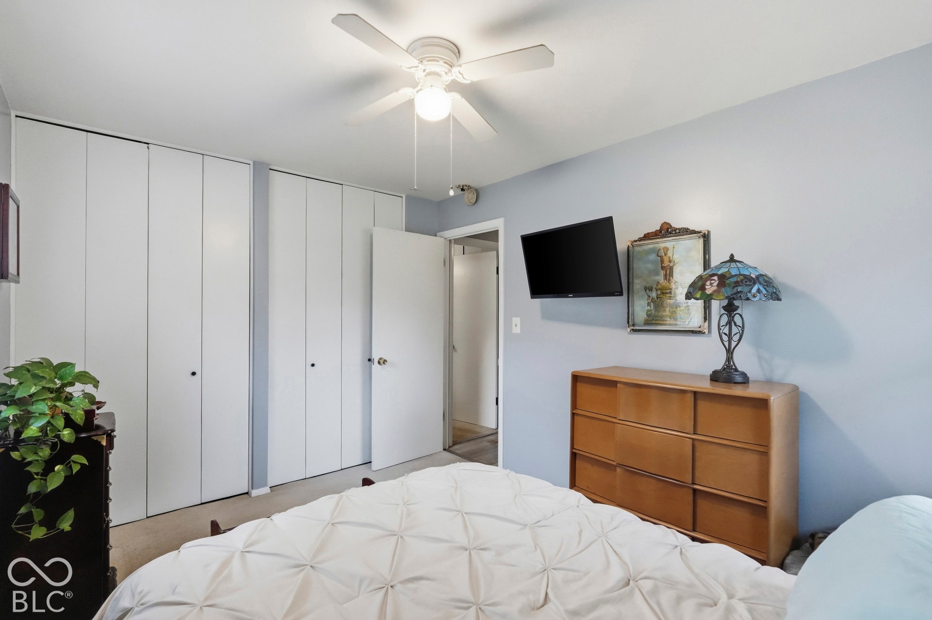 Another view of the bedroom featuring white bi-fold closet doors and a ceiling fan with integrated light fixture. The floor is carpeted.
