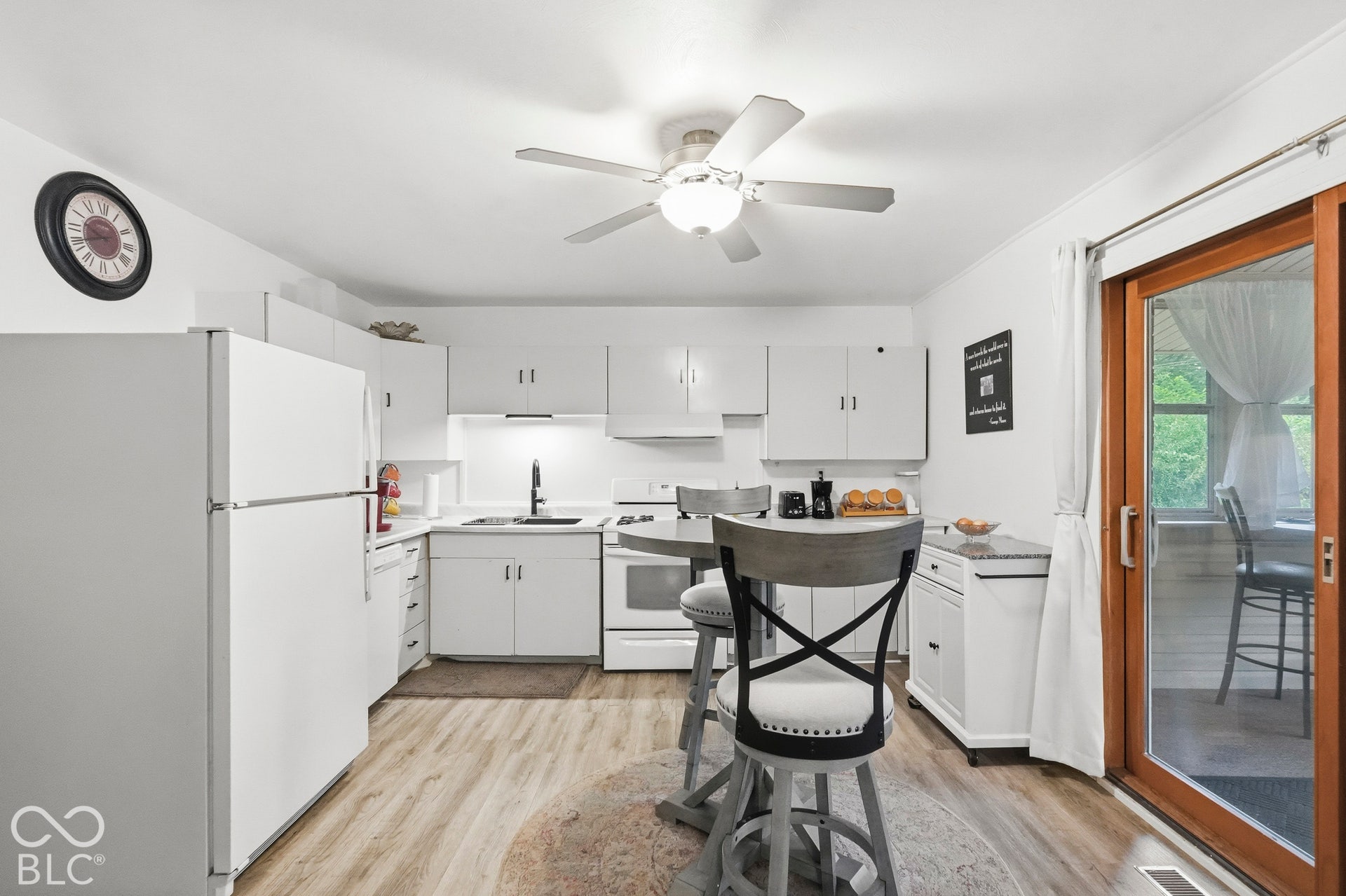 Kitchen featuring white cabinetry, vinyl plank flooring, the range, the top-freezer refrigerator, and a sliding glass door that leads to the spacious sun room.