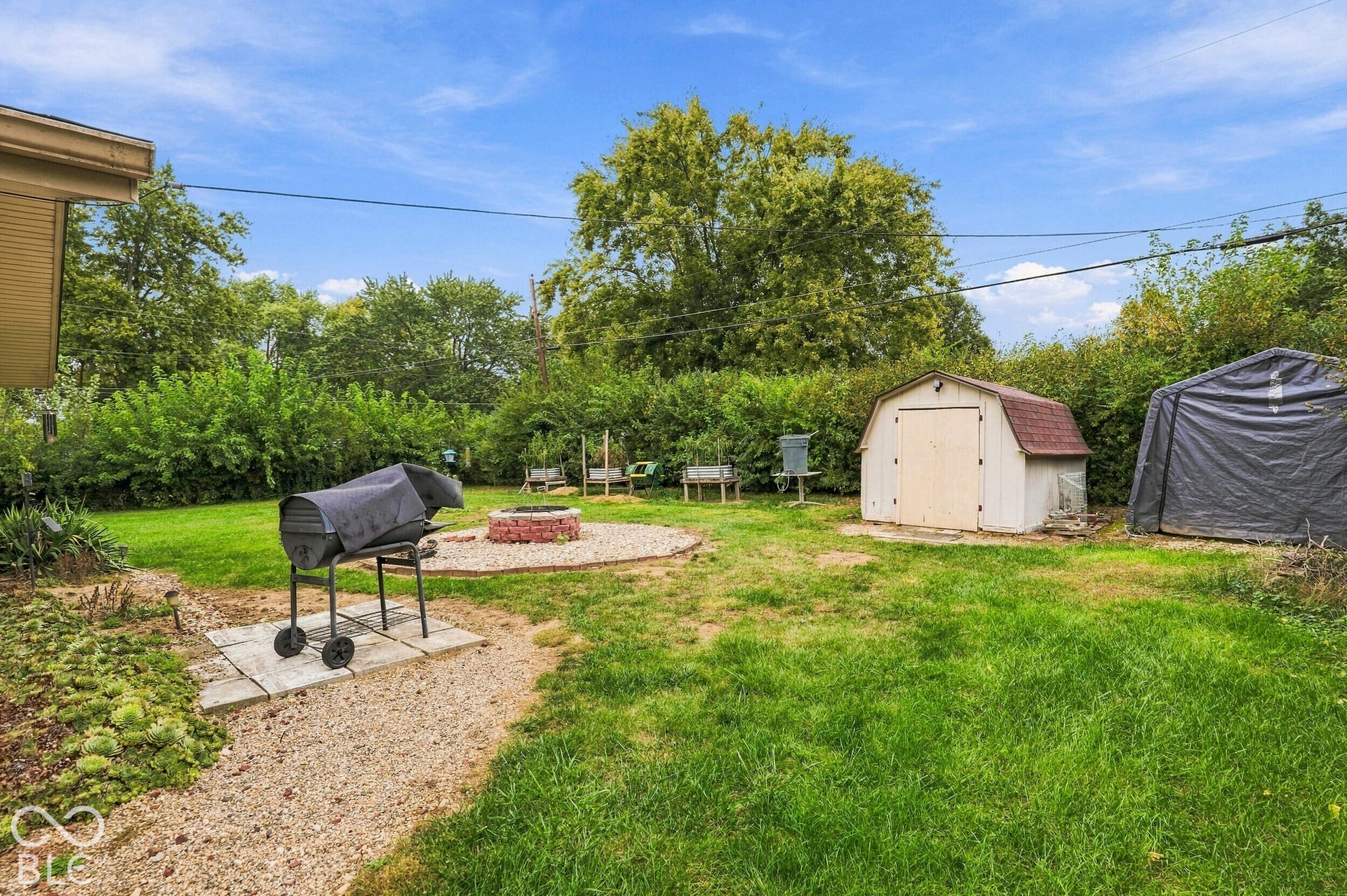 The backyard space features a lawn, a brick-surrounded fire pit, and two storage sheds. The back yard is very private due to the Rose of Sharon bushes.