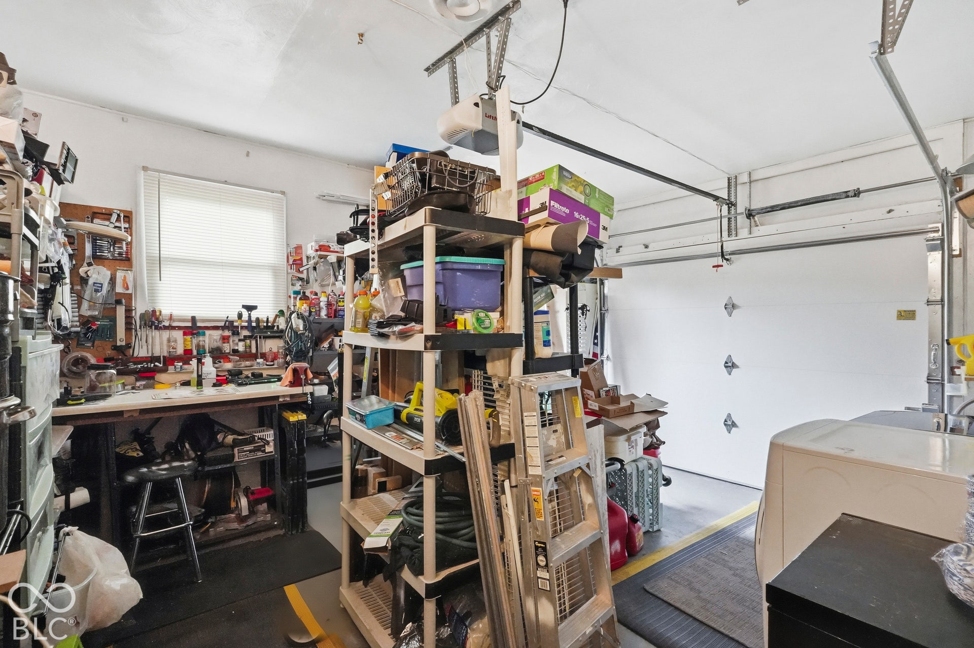 The garage features a paneled overhead door, remote control door opener, a southerly window for natural light, and integrated utility work area. The space is currently storing tools to move.