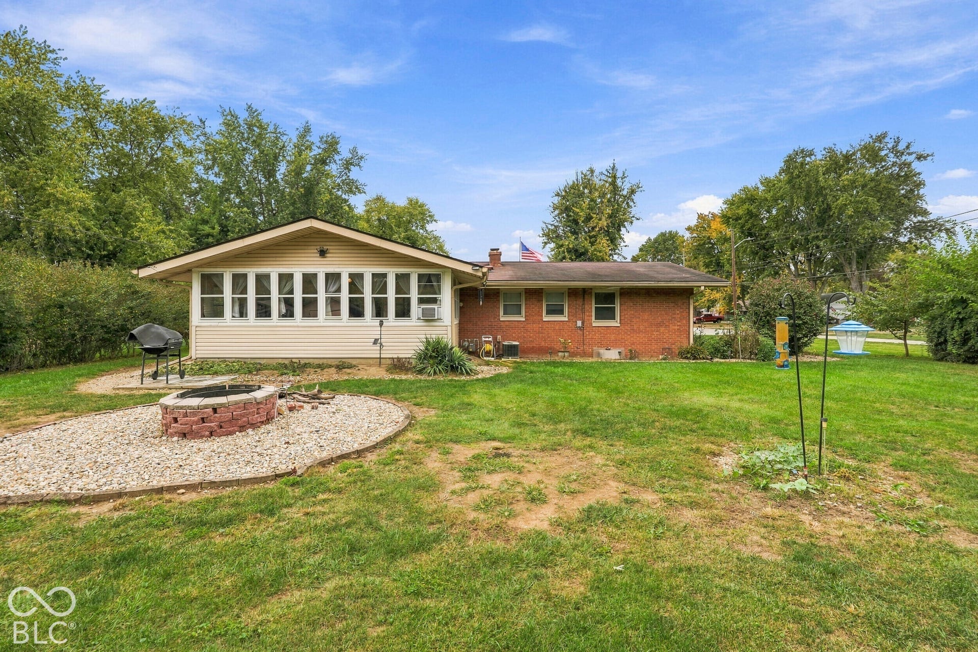 Rear exterior featuring the brick and siding facade, the sunroom with large windows, and the gravel fire pit.