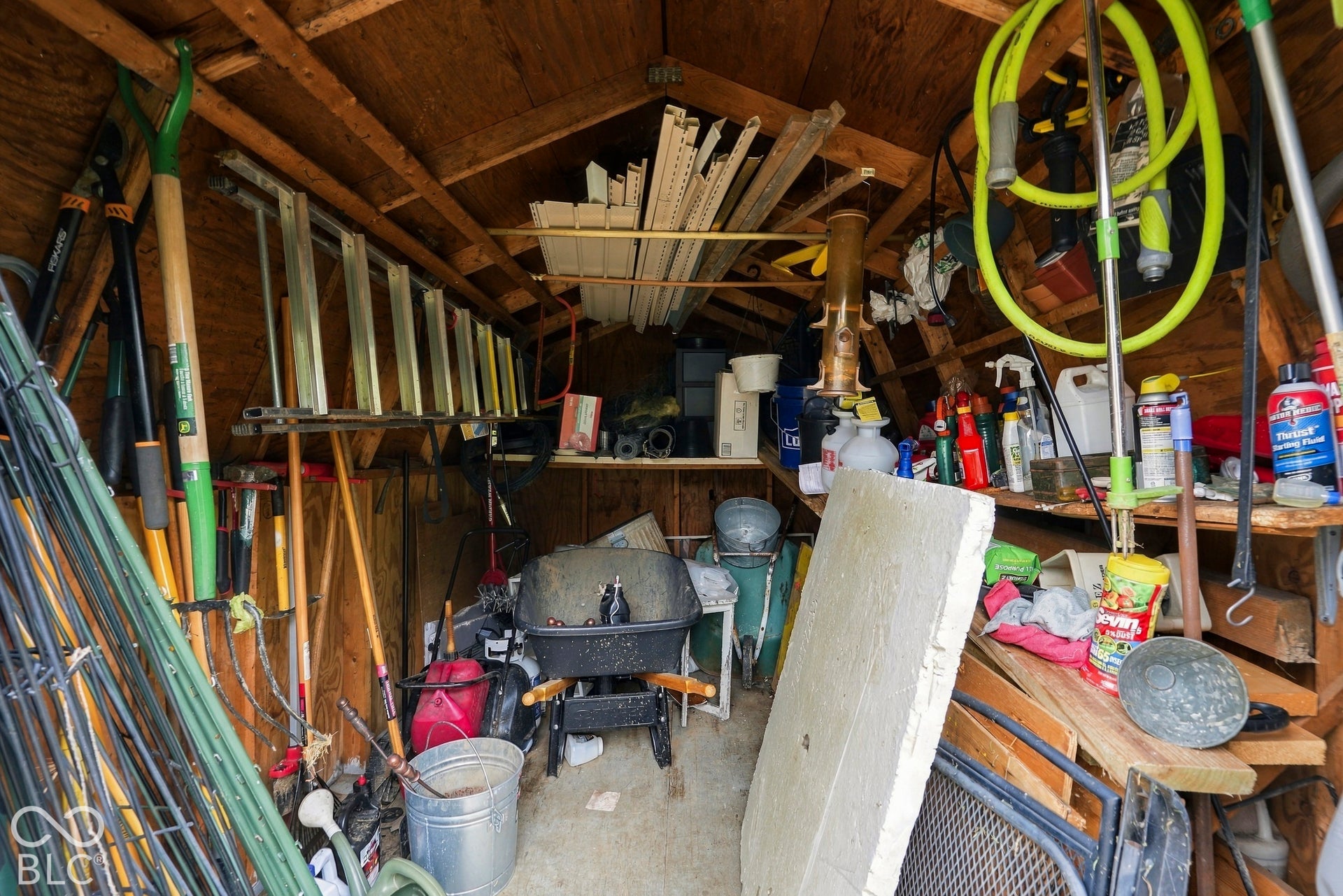 The storage shed with exposed wood framing, built-in shelving, and concrete flooring will store all of your yard care equipment throughout the year.