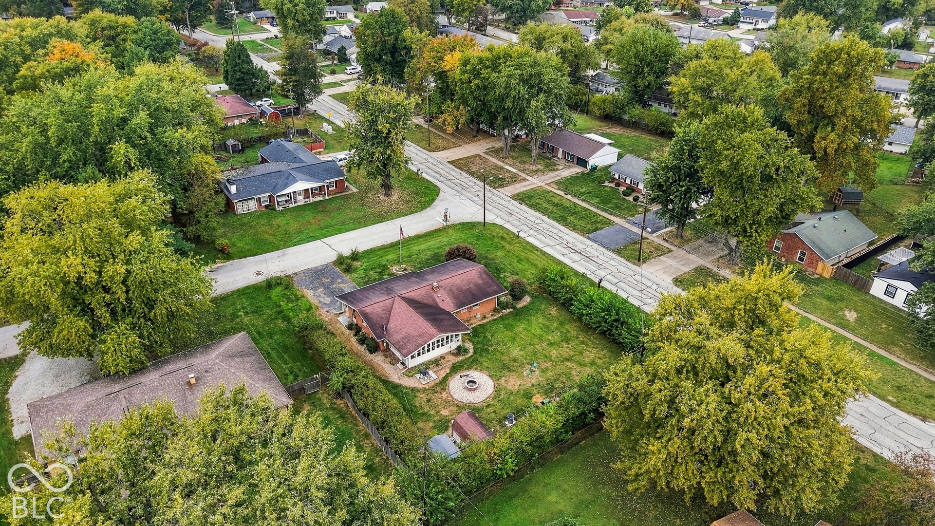 Aerial perspective of the detached single-story home situated on a corner lot, featuring mature trees, and a concrete driveway