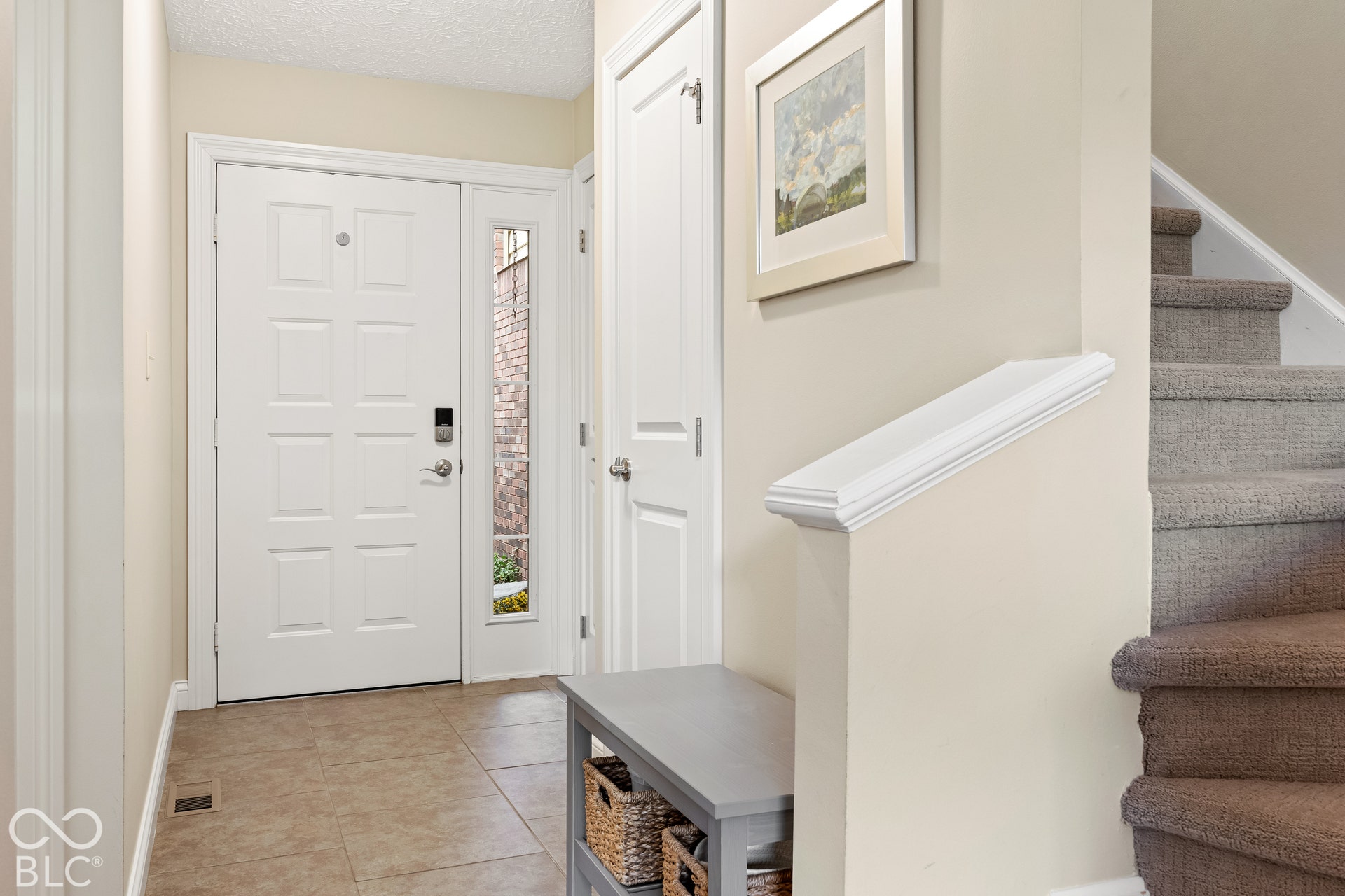 Entryway featuring a white paneled front door with a side window light, neutral tile flooring, and carpeted stairs with a white handrail