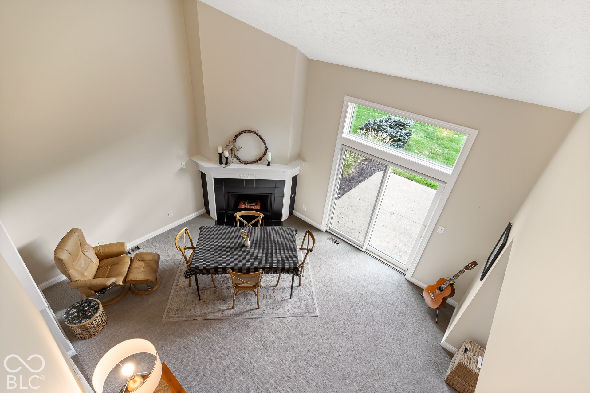 Vaulted ceiling with an open floor plan, corner fireplace featuring a white mantel and black tile surround, and sliding glass doors with a transom window