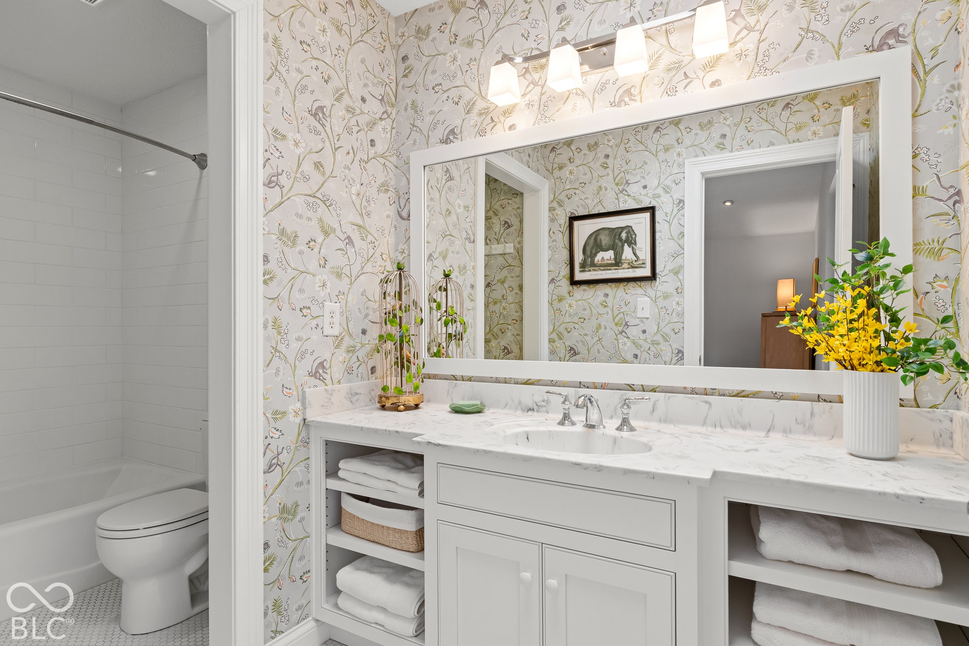 Bathroom featuring stone-surface vanity with an integrated oval basin, white cabinetry with open shelving, a large framed wall mirror, multi-bulb overhead lighting, and a shower-tub combination with white subway-style wall tile