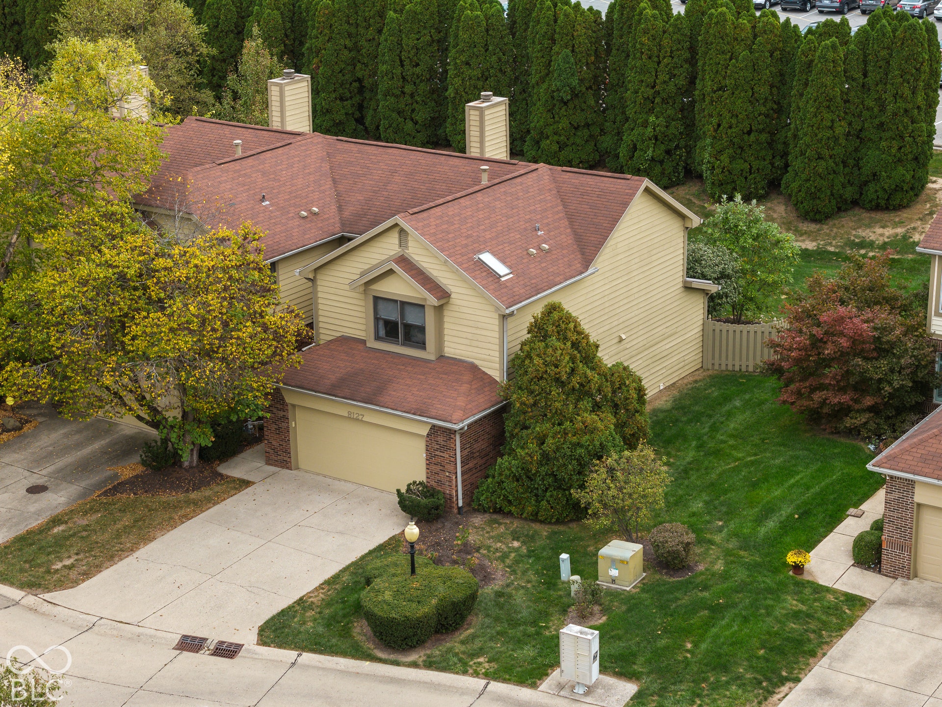 Two-story exterior featuring tan horizontal siding, brick masonry detailing, an attached two-car garage, multiple chimneys, and a shingled roof