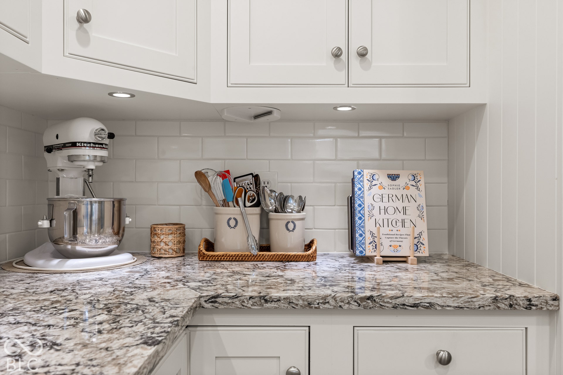 White shaker-style cabinetry with satin nickel hardware, polished stone-finish countertops, subway tile backsplash, and recessed under-cabinet lighting