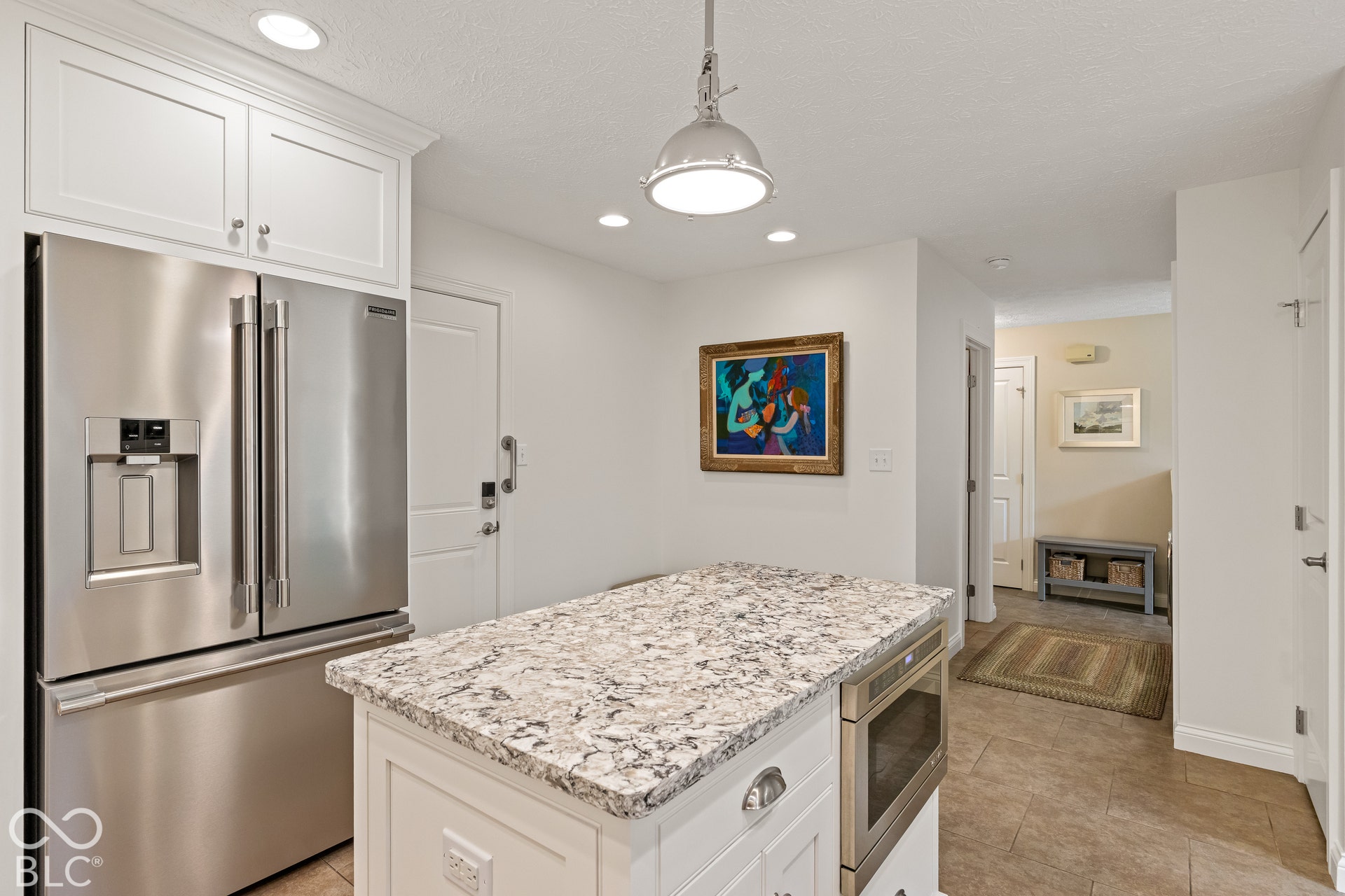 Kitchen featuring an island with a stone-finish countertop, stainless steel refrigerator, built-in microwave, white shaker-style cabinetry, and recessed lighting
