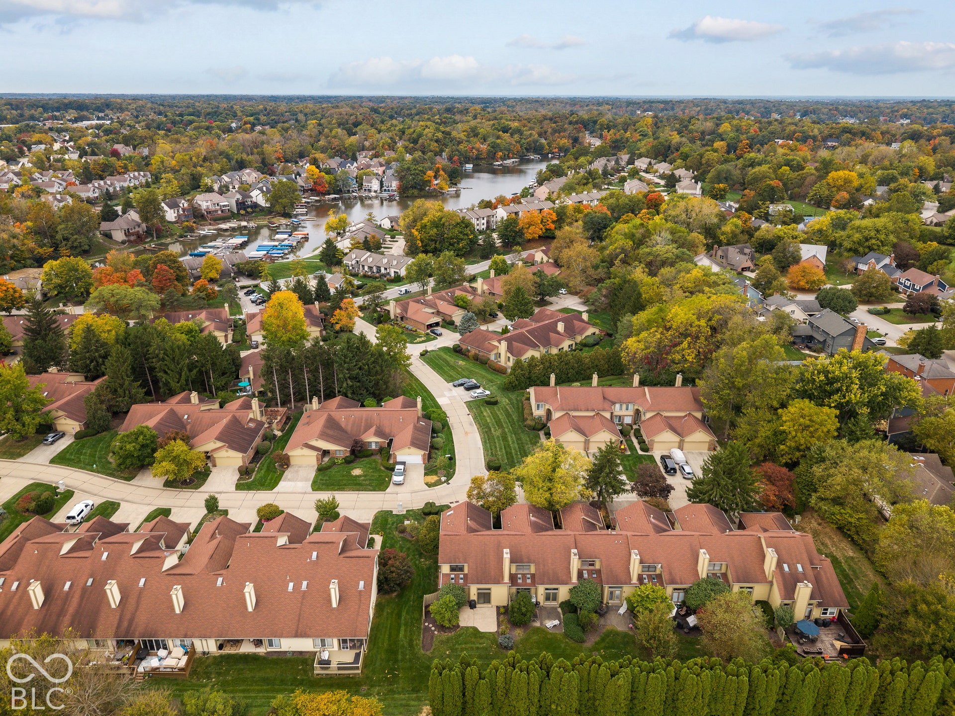 Aerial perspective of a multi-unit residential community featuring shingled rooflines, paved access roads, private concrete patios, and established landscaping with mature trees