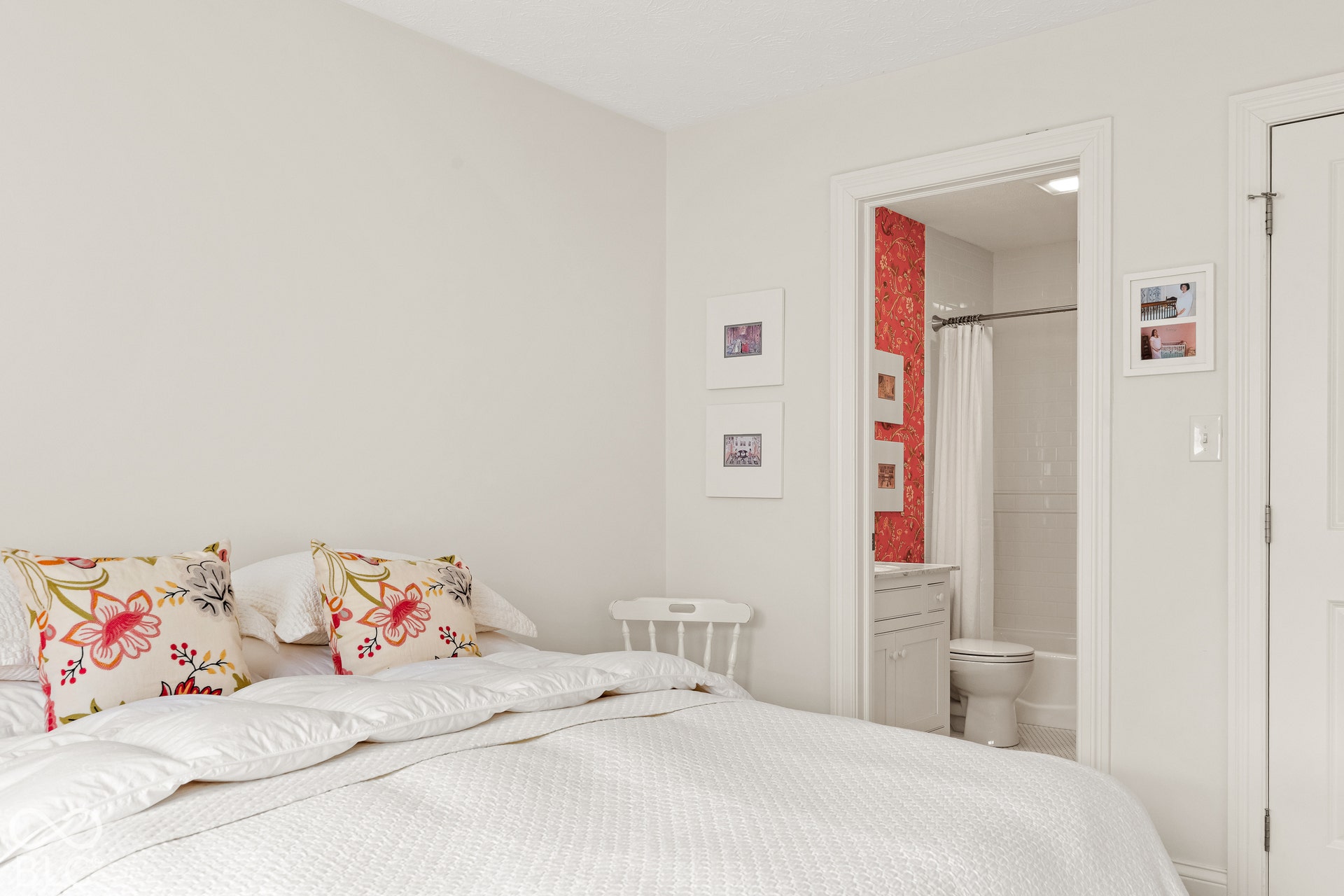 Neutral-toned room with white interior door featuring casing trim and en-suite bath containing a white cabinet vanity and tub-shower combination with patterned wall covering