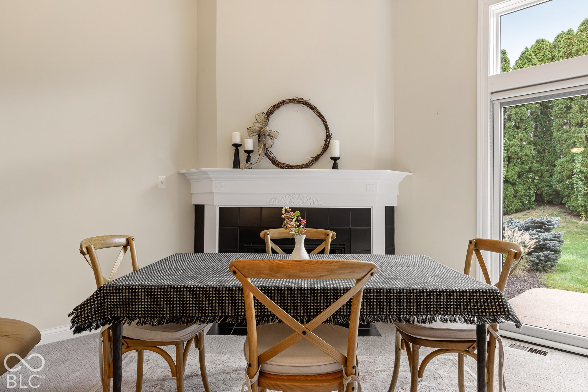Fireplace with a white mantel and black tile surround, high ceilings, and large windows with exterior foliage