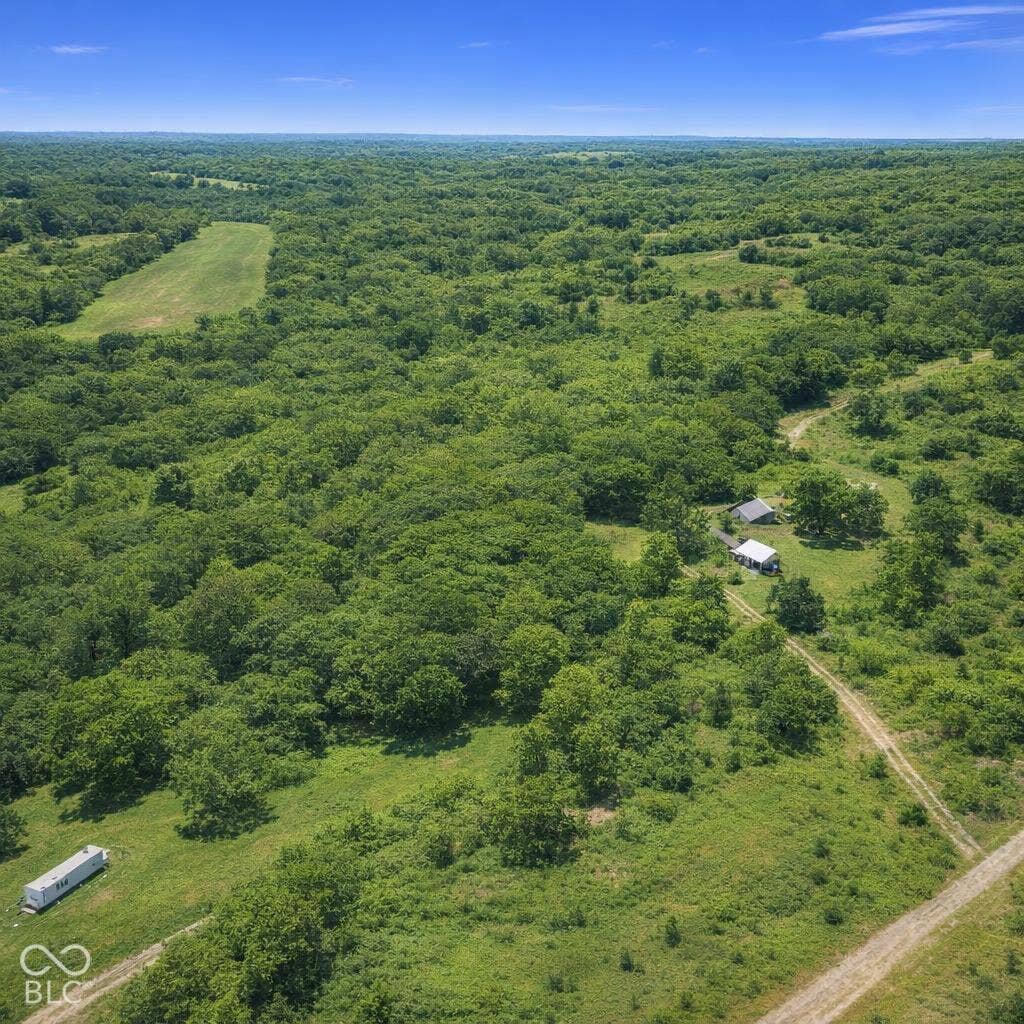 Expansive acreage featuring mature tree lines, rolling meadows, private gravel access paths, and multiple permanent outbuildings