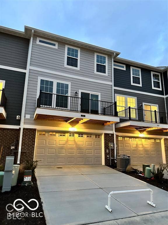 Multi-story exterior featuring a mix of horizontal lap siding and brick masonry, second-story balcony with metal railings, and an attached two-car garage with a concrete driveway
