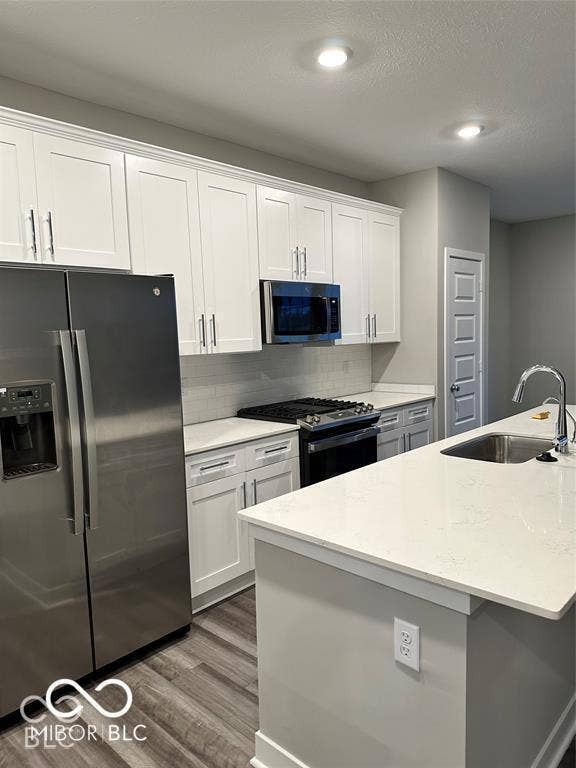 Kitchen featuring white shaker-style cabinetry, stainless steel appliances, a central island with a quartz countertop, and wood-finish flooring