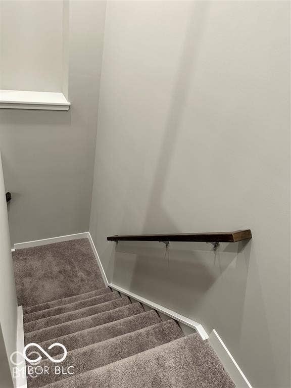 Staircase featuring wall-to-wall carpeting and a dark-stained wooden handrail with metal mounting brackets
