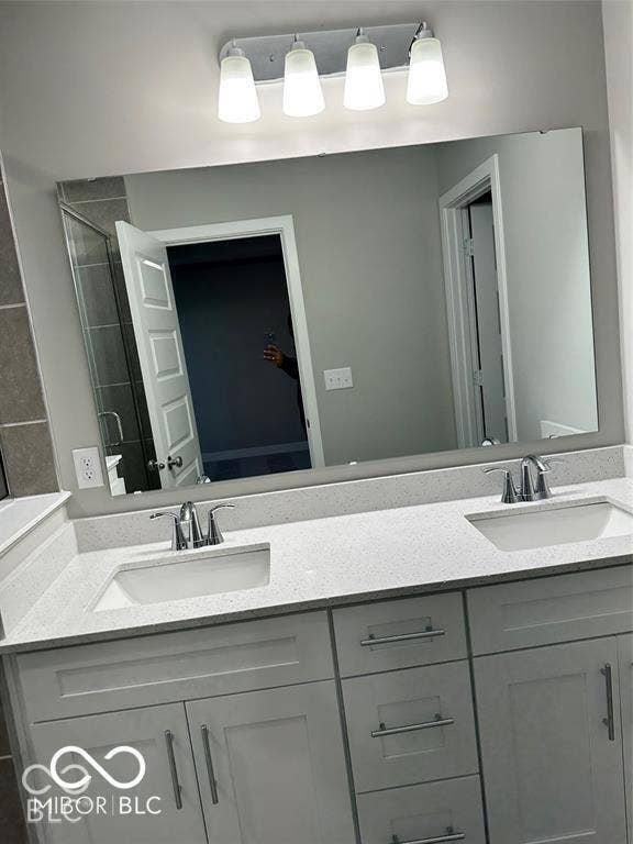 Double vanity featuring Shaker-style cabinetry, a solid surface countertop with dual undermount sinks, chrome fixtures, and a four-light vanity fixture