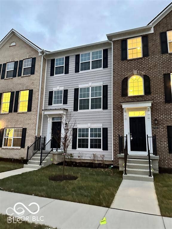 Multi-story exterior featuring a combination of brick and horizontal siding, multi-pane windows with black shutters, arched window detailing, and metal-railed concrete entry steps