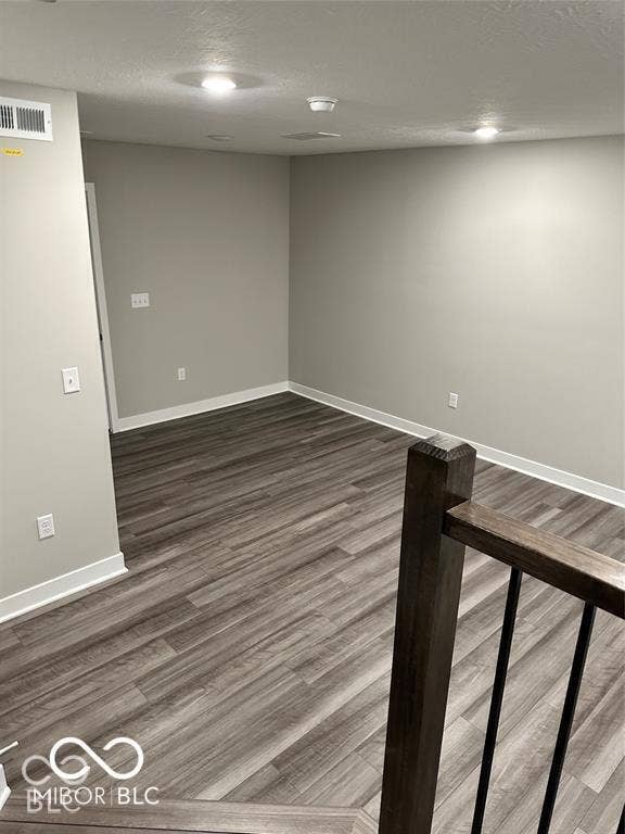 Interior space featuring wood-finish flooring, neutral wall paint, and recessed lighting, accompanied by a staircase with a dark wood handrail and metal balusters