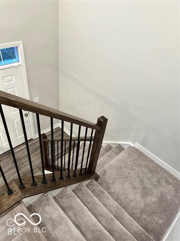 Staircase featuring carpeted steps, a dark-stained wood handrail, and matte black vertical metal balusters