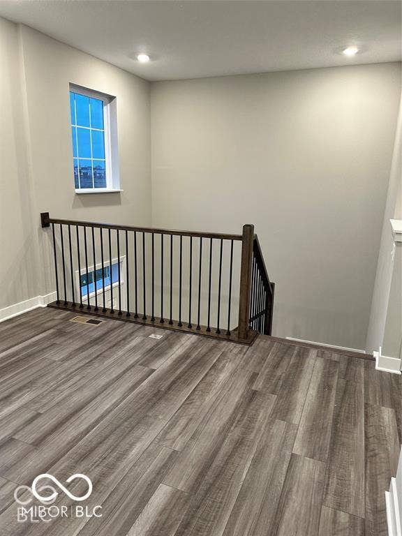 Wood-finish flooring featuring a dark railing with vertical metal balusters, recessed ceiling lighting, and a multi-pane window