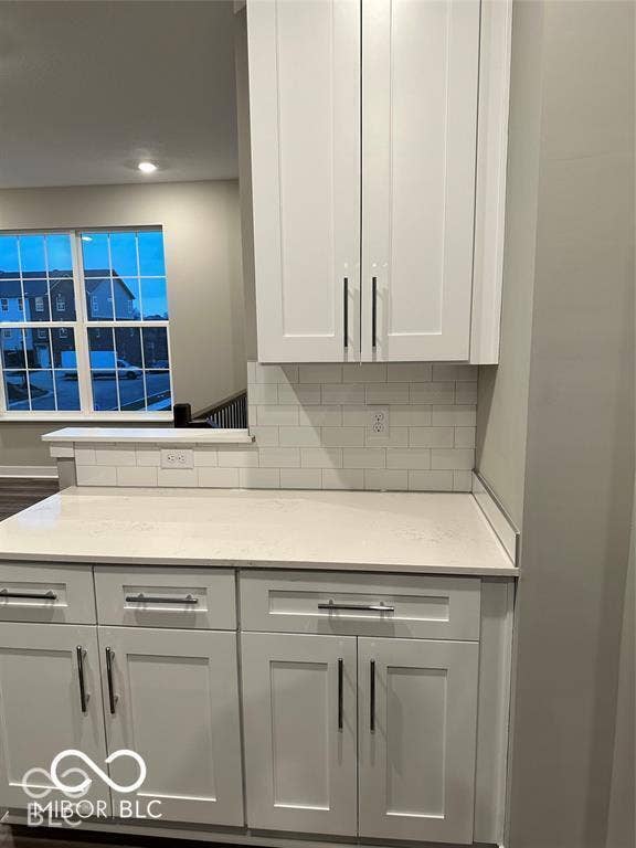 White shaker-style cabinetry with matte black hardware, stone-composite countertops, and a white subway tile backsplash