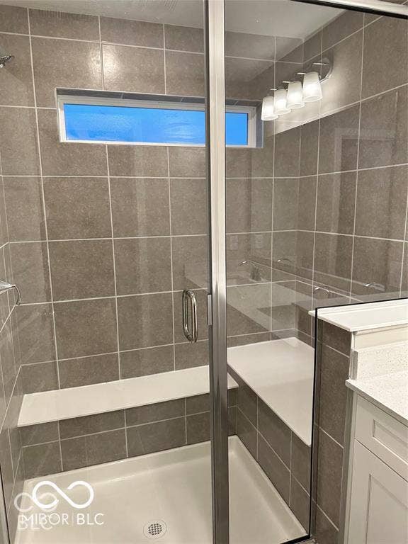 Walk-in shower featuring large-format ceramic wall tile, a built-in tiled bench, a glass enclosure with brushed metal hardware, and a transom window