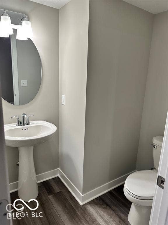 Pedestal sink with chrome faucet, oval wall-mounted mirror, two-light fixture, and wood-finish flooring