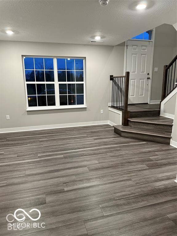 Wood-finish flooring, recessed lighting, multi-pane window, and staircase featuring stained-wood railings with metal balusters