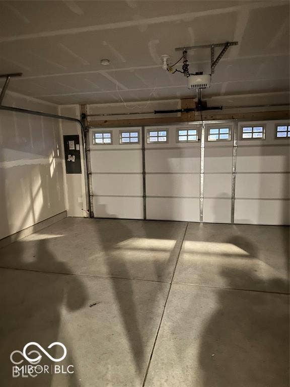 Garage featuring a concrete floor, finished drywall, overhead door with paneled windows, and automatic door opener