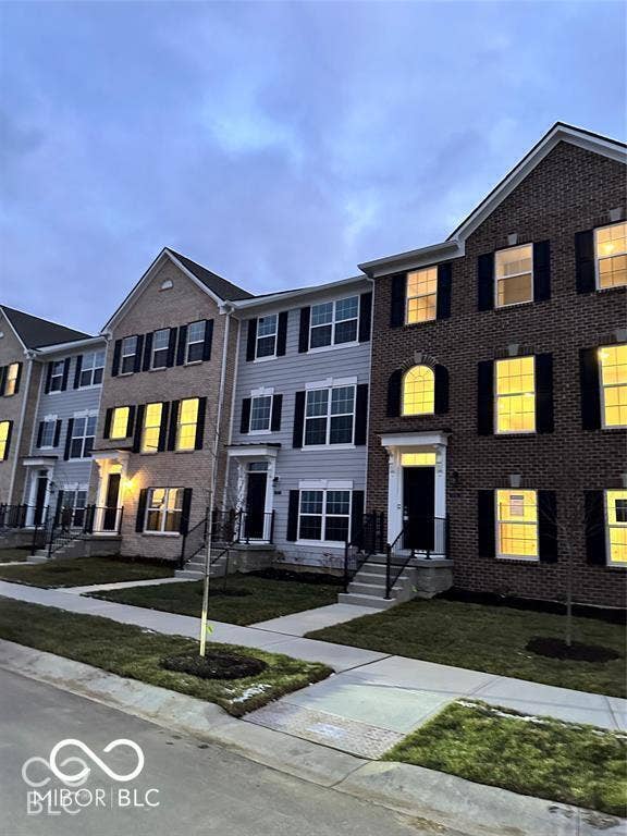 Multi-story townhome exterior featuring a combination of brick and horizontal siding, decorative shutters, arched window accents, and concrete entry steps with metal railings