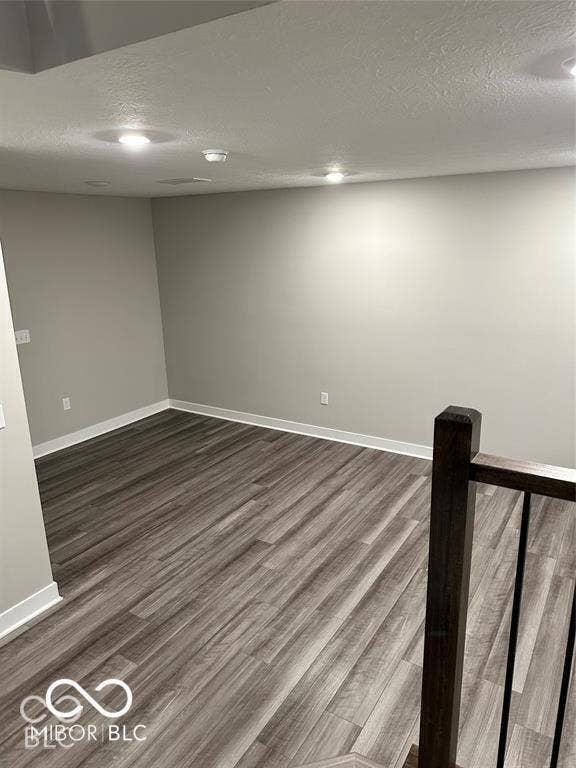 Neutral wall finishes, wood-finish flooring, and integrated recessed lighting, accented by a dark wood-finish railing with metal balusters