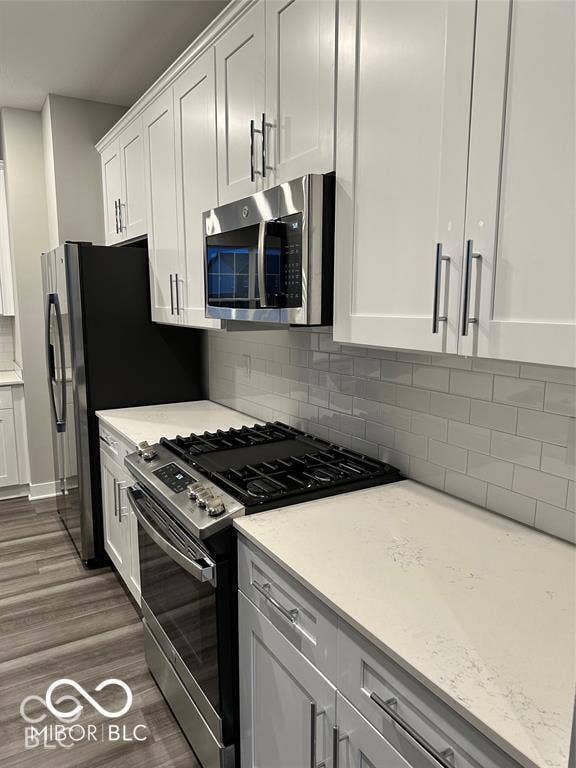 White cabinetry with brushed nickel hardware, stone-finish countertops, subway tile backsplash, stainless steel appliances, and wood-finish flooring
